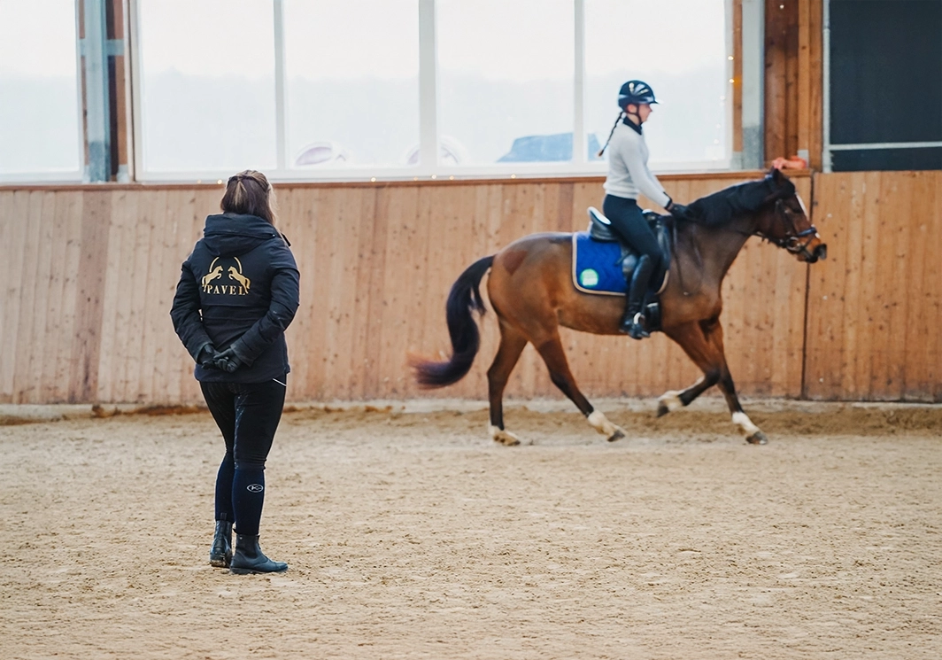 Reitlehrerin beobachtet Schülerin auf Pferd in Reithalle