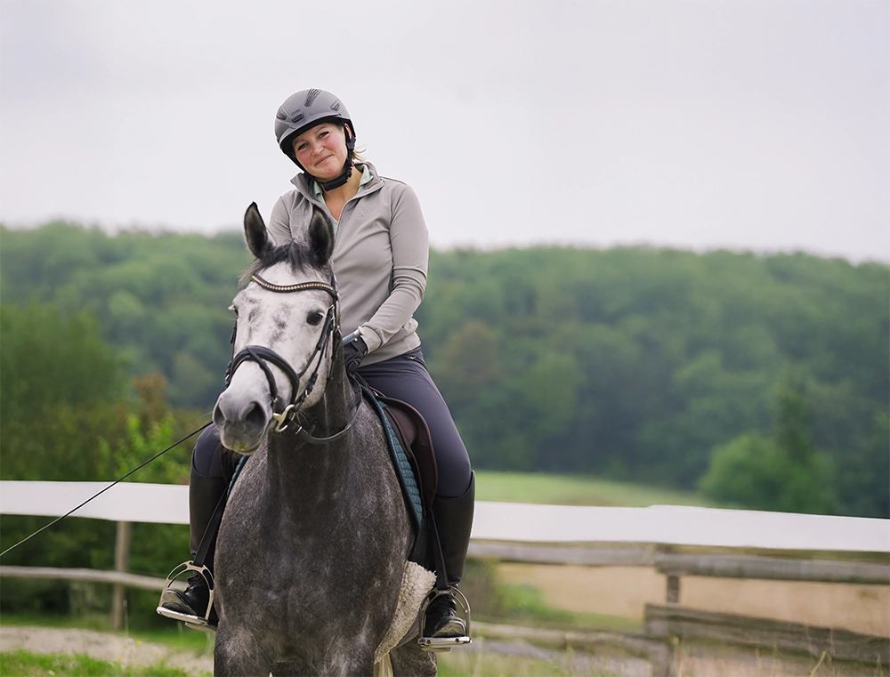 Mitarbeiterin des Reitstall Pavel beim Beritt eines Pferdes, lächelt in die Kamera.